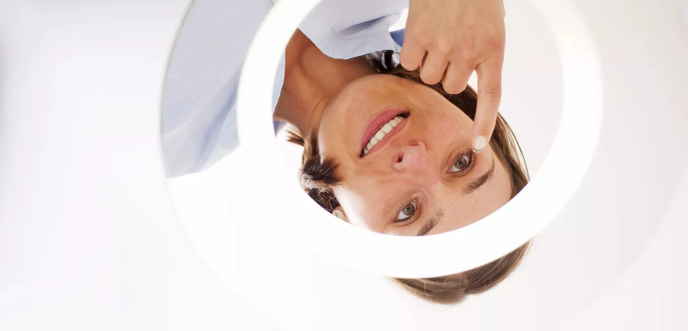 Frau schaut in Spiegel zum Kontaktlinse einsetzen