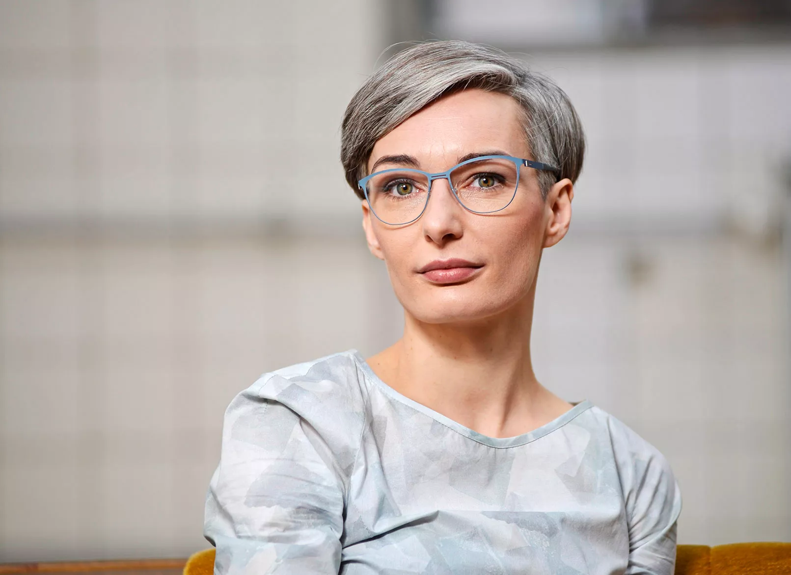 Junge Frau mit grauen kurzen Haaren und einer modernen Brille, die in die Kamera schaut