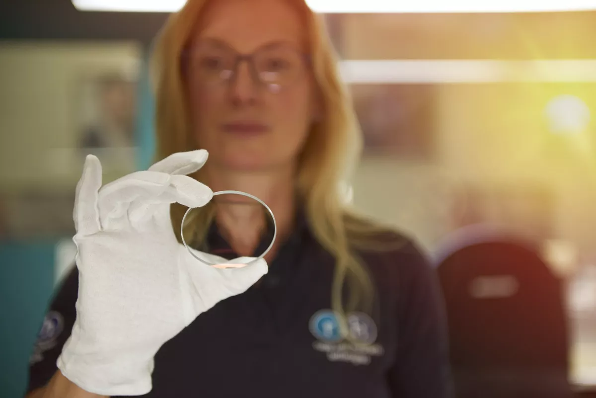 Brillenglas beim Hersteller wird kontrolliert von einer Frau mit weißem Handschuh
